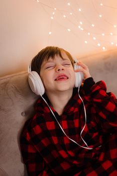 A boy with headphones is lying on the sofa lifestyle. The boy listens to music. New Year's mood.