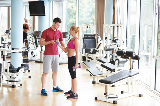 young sporty woman with trainer exercise weights lifting in fitness gym