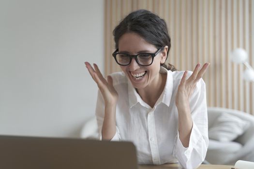 Motivated Italian female tutor in formal wear and glasses sits at desk at home against web cam lecturing training webinar online. Portrait of joyful coach lady looks at laptop screen while communicate