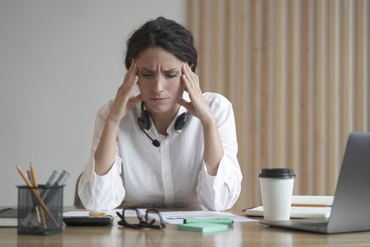 Stressed young entrepreneur lady suffering from headache massaging temples while sitting at home office, tired female freelancer feeling unwell, touching head. Migraine pain, fatigue, stress concept