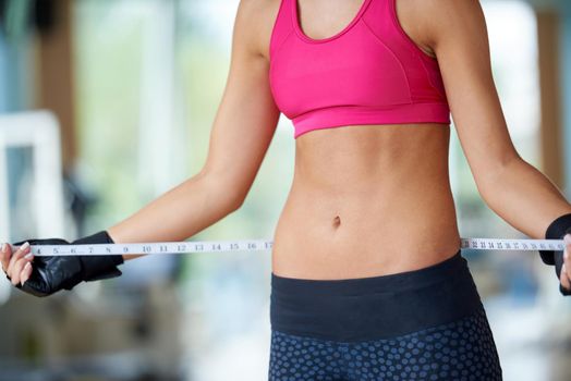 young fit woman measuring belly on a training  in  fitness gym