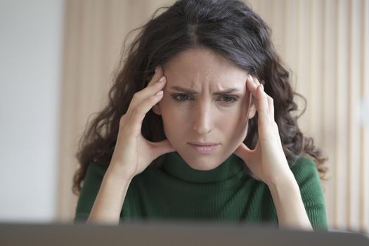 Concerned young italian woman employee looking at laptop computer screen with frustrated face expression, reading bad news by email, worried female office worker thinking of problem solution at work