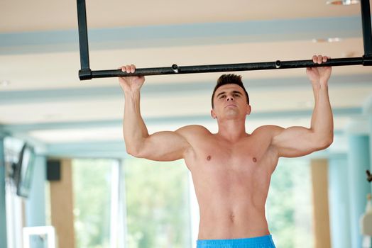 handsome young man in fitness gym lifting up and hanging while working on hands and back muscles