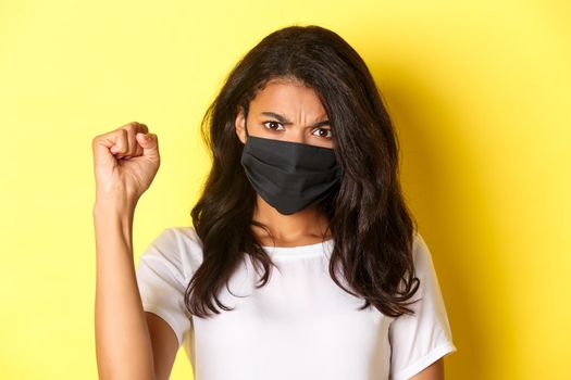 Concept of covid-19, social distancing and lifestyle. Close-up of fierce and confident african-american woman, being a protester in black lives matter movement, showing a fist, wearing face mask.