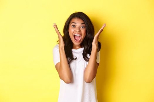 Image of young african american woman looking annoyed, screaming bothered and angry, standing over yellow background.