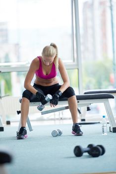 halethy young woman exercise with dumbells and relaxing on banch in fitness gym