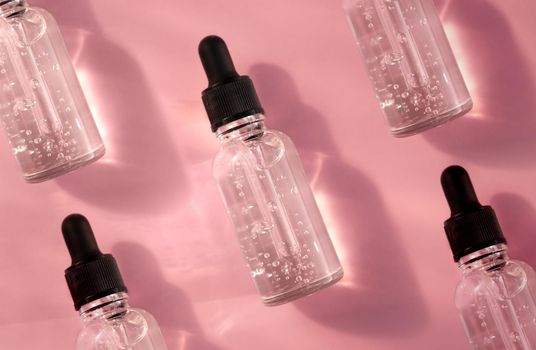 Transparent glass dropper bottle with air bubbles pattern on pink background in sunlight. Pipette with fluid hyaluronic acid, serum, retinol. Cosmetics and healthcare concept. Luxury beauty product