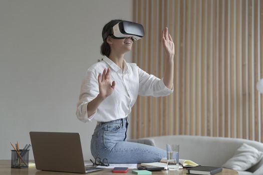 Employee experience with virtual reality. Impressed business woman sitting on office table, using vr glasses goggles at work, testing innovative method for business, interacting with digital interface