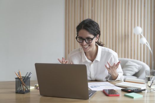 Overjoyed italian business woman reading great news on laptop at her workplace, happy female employee wearing glasses receiving good email, celebrating business success while sitting at office desk