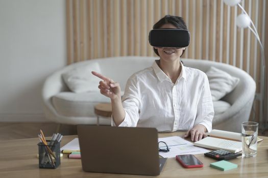 Female office worker wearing vr headset or virtual reality goggles touching objects in cyberspace or digital world, using innovative technologies for business at work, dressed in formal outfit