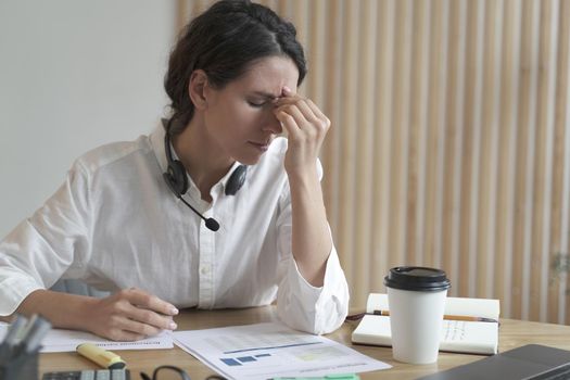 Tired spanish female home office worker massages nose or inner corners of her eyes, suffers from chronic daily headache and high pressure after all day of work at computer. Fatigue and stress concept