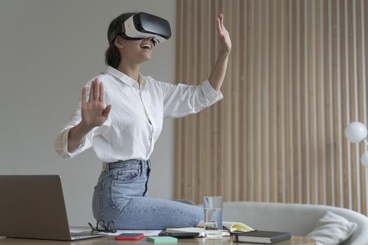 Future technologies. Young amazed businesswoman in virtual reality glasses testing innovative method for business, sitting on desk at her workplace and using VR goggles while working remotely at home
