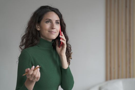 Attractive Spanish young businesswoman enjoying telephone conversation with partner, woman using modern smartphone at work, smiling female office worker consulting client via mobile