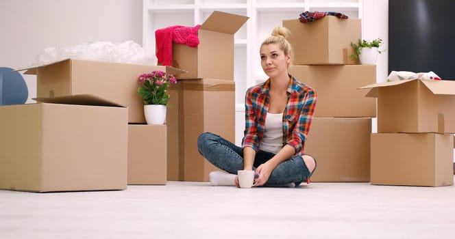 people, moving new place and repair concept   happy beautiful  young woman with many cardboard boxes sitting on floor with Cup at home