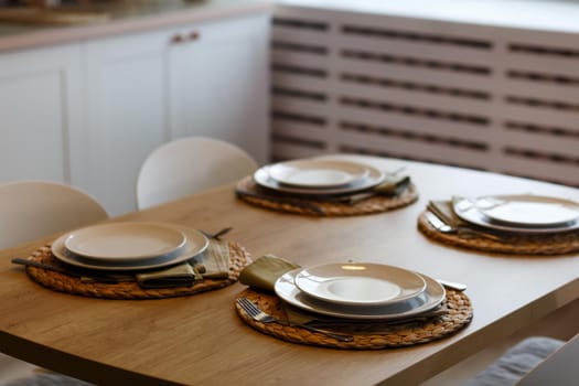 White plates with stainless steel spoons and forks on the plate mats on wooden table.