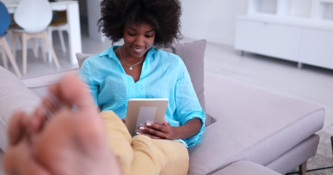 Young african american woman at home relaxing in her luxury lliving room reading a digital tablet PC surf internet and work