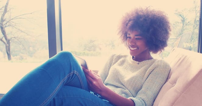 Young african american woman at home relaxing in her luxury lliving room reading a digital tablet PC surf internet and work