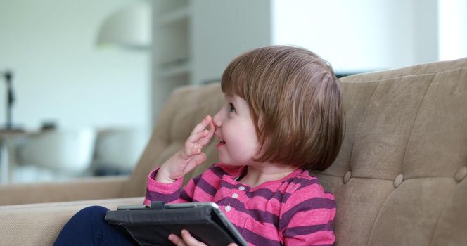 Cute little girl  sitting on coutch and using touchpad or tablet and smiling