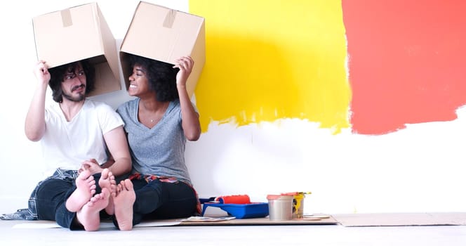 Happy young multiethnic couple relaxing and playing with cardboard boxes after painting a room in their new house on the floor