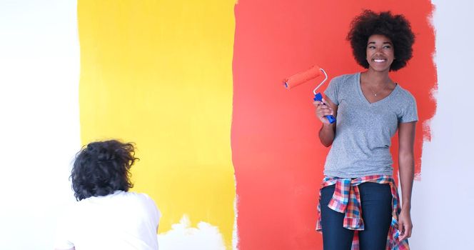 happy young multiethnic couple painting interior wall of new house