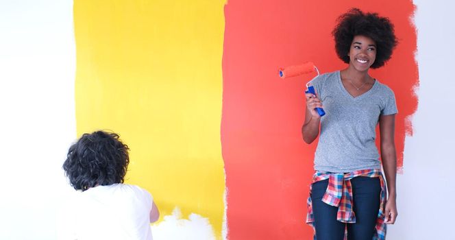 happy young multiethnic couple painting interior wall of new house