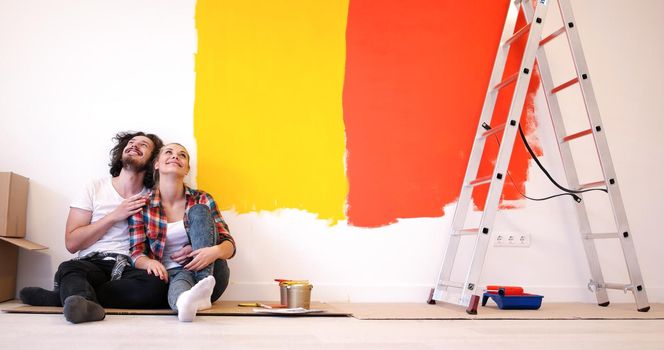 Happy young couple relaxing after painting a room in their new house on the floor