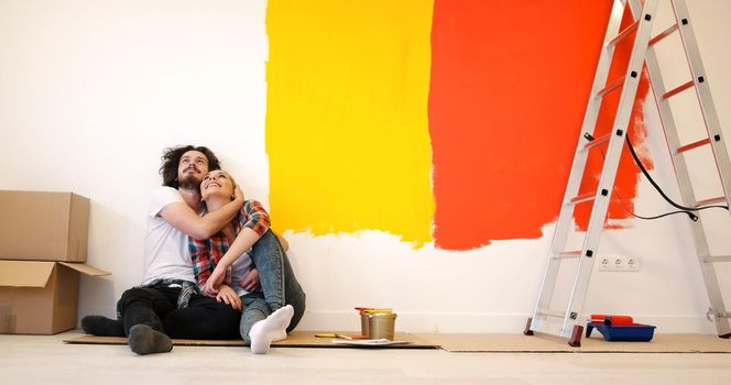 Happy young couple relaxing after painting a room in their new house on the floor