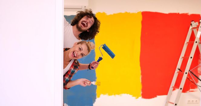 portrait of happy smiling young couple painting interior wall of new house  peeking from behind the wall