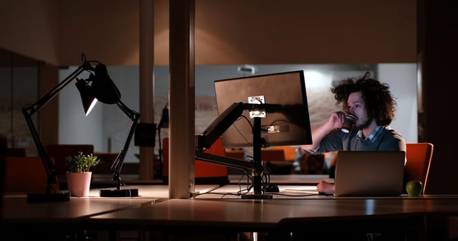 Young man working on computer at night in dark office. The designer works in the later time.