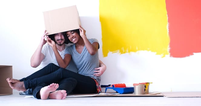 Happy young multiethnic couple relaxing and playing with cardboard boxes after painting a room in their new house on the floor