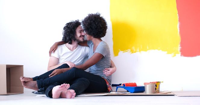 Happy young multiethnic couple relaxing after painting a room in their new house on the floor