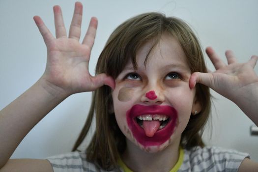 Cute little preschool girl playing with mommy's make up. Fashion experiment little child applying makeup lipstick and shadow on face, staying at home in corona virus quarantine.