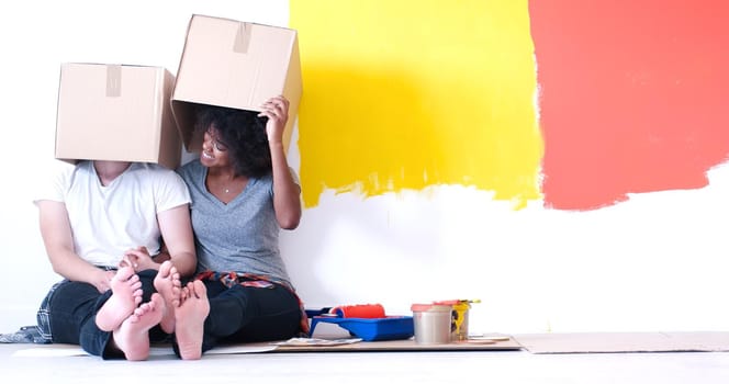 Happy young multiethnic couple relaxing and playing with cardboard boxes after painting a room in their new house on the floor