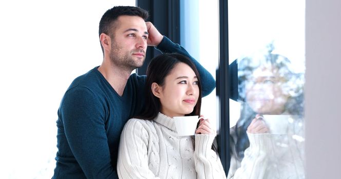 young multiethnic romantic couple enjoying morning coffee by the window in their luxury home