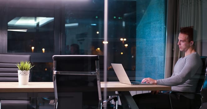 Young man working on laptop at night in dark office. The designer works in the later time.