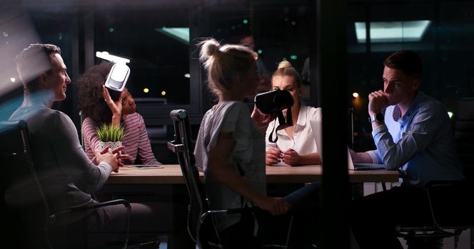 Multiethnic Business team using virtual reality headset in night office meeting  Developers meeting with virtual reality simulator around table in creative office.