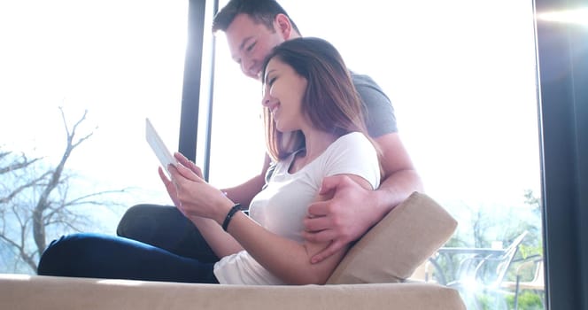 Young couple relaxing at luxurious home with tablet computers reading in the living room on the sofa couch.