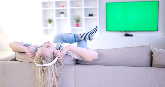 Young beautiful girl enjoying music through headphones, laying on sofa at home