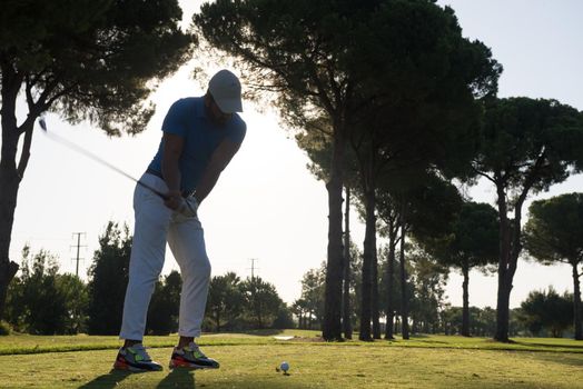 golf player hitting shot with club on course at beautiful morning with sun flare in background