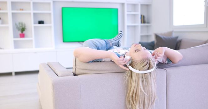 Young beautiful girl enjoying music through headphones, laying on sofa at home