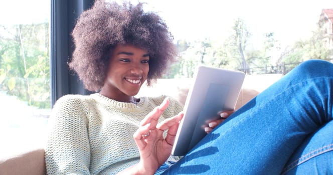 Young african american woman at home relaxing in her luxury lliving room reading a digital tablet PC surf internet and work