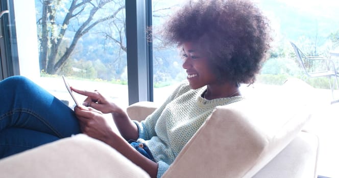 Young african american woman at home relaxing in her luxury lliving room reading a digital tablet PC surf internet and work