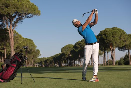 golf player hitting shot with club on course at beautiful morning with sun flare in background