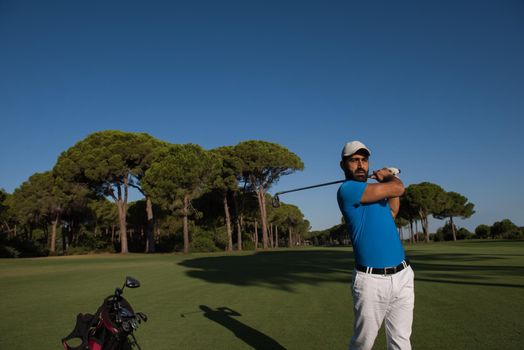 golf player hitting shot with club on course at beautiful morning with sun flare in background