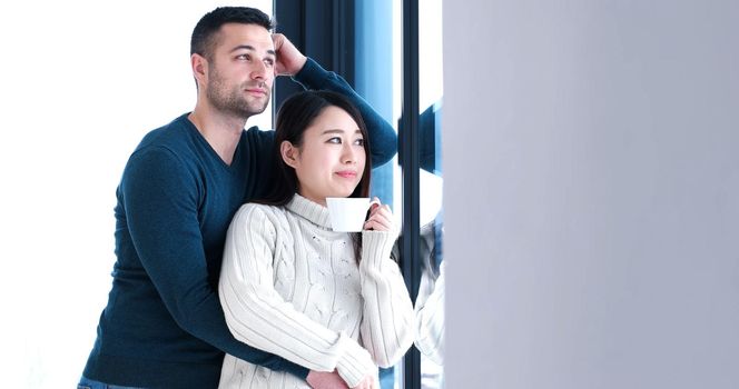 young multiethnic romantic couple enjoying morning coffee by the window in their luxury home