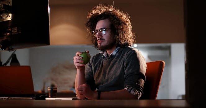 Young man working on computer at night in dark office. The designer works in the later time.