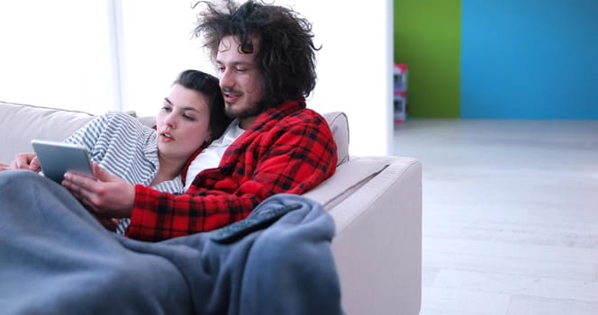 Young couple relaxing at luxurious home with tablet computers reading in the living room on the sofa couch.