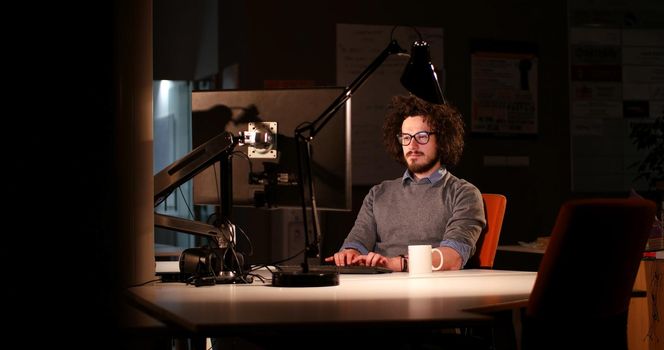 Young man working on computer at night in dark office. The designer works in the later time.