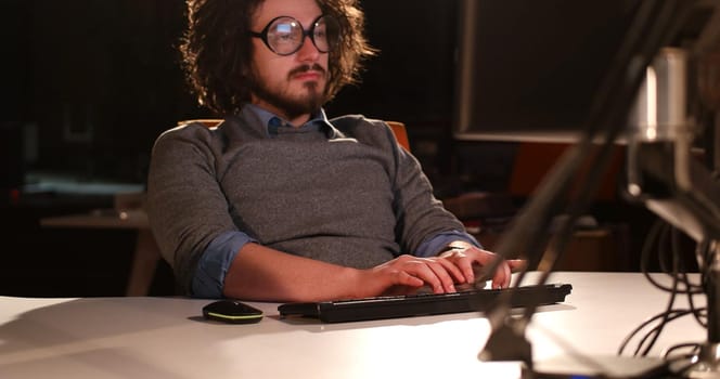 Young man working on computer at night in dark office. The designer works in the later time.