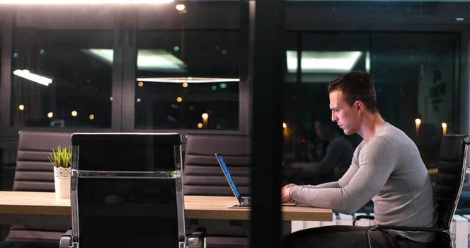 Young man working on laptop at night in dark office. The designer works in the later time.